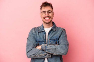 Pembe arka planda izole edilmiş genç beyaz adam kendini güvende hissediyor, kararlılıkla kollarını kavuşturuyor..