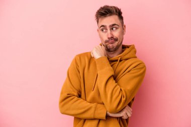 Pembe arka planda soyutlanmış, kafası karışmış, şüpheli ve kararsız genç bir beyaz adam..