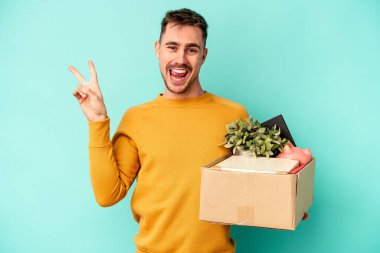 Kafkasyalı genç bir adam mavi arka planda izole edilmiş bir hareket yapıyor neşeli ve tasasız parmaklarıyla barış sembolü gösteriyor..