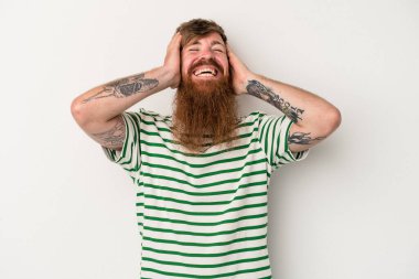 Beyaz arka planda uzun sakallı beyaz tenli genç beyaz adam ellerini başının üstünde tutarak neşeyle gülüyor. Mutluluk kavramı.