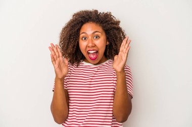 Beyaz arka plandaki kıvırcık saçlı genç Afrikalı Amerikalı kadın zaferi ya da başarıyı kutluyor, şaşırdı ve şok oldu..