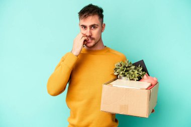 Kafkasyalı genç bir adam mavi arka planda izole edilmiş tırnak yiyor, gergin ve endişeli..