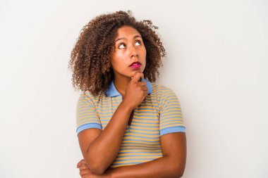 Beyaz arka planda yalıtılmış kıvırcık saçlı, şüpheli ve şüpheci bir ifadeyle yan bakan Afro-Amerikalı genç bir kadın..