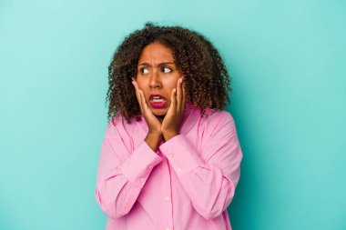Kıvırcık saçlı genç Afrikalı Amerikalı kadın mavi arka planda izole edilmiş korkmuş ve korkmuş..
