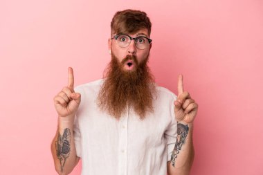 Uzun sakallı, beyaz, genç bir adam pembe arka planda izole edilmiş. Ağzı açık, üst tarafı işaret ediyor..