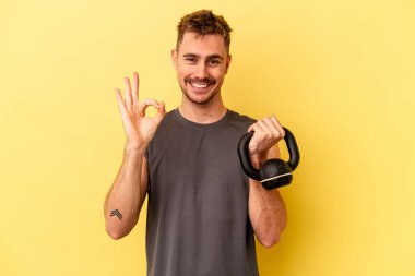 Sarı arka planda izole edilmiş bir halter tutan genç sporcu neşeli ve kendinden emin..