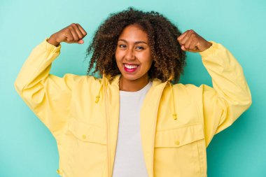 Mavi arka planda yalıtılmış kıvırcık saçlı, genç Afro-Amerikalı kadın güçlü bir hareket gösteriyor, kadınsı gücün sembolü.