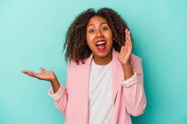 Mavi arka planda izole edilmiş kıvırcık saçlı Afro-Amerikalı genç bir kadın avuç içinde fotokopi alanı tutuyor, el üstünde tutuyor. Şaşırmış ve mutlu..