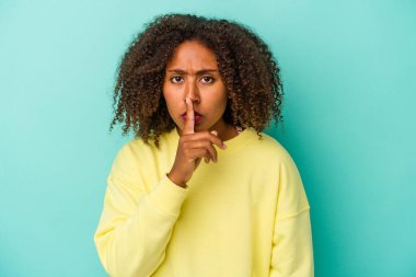 Mavi arka planda yalıtılmış kıvırcık saçlı, genç Afro-Amerikalı bir kadın ya sır saklıyor ya da sessizlik istiyor..