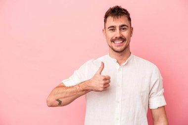 Pembe arka planda izole edilmiş genç beyaz adam gülümsüyor ve başparmağını kaldırıyor.