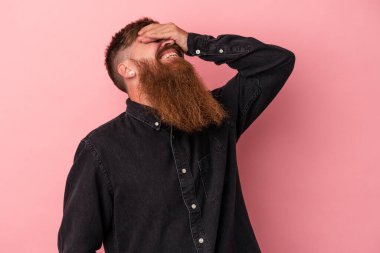 Pembe arka planda uzun sakallı, beyaz, genç bir adam ellerini başının üstünde tutarak gülüyor. Mutluluk kavramı.