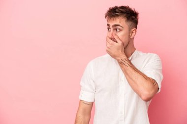 Pembe arka planda izole edilmiş genç beyaz bir adam. Düşünceli bir şekilde ağzıyla ağzını kapatan bir fotokopi odasına bakıyor..
