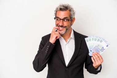 Orta yaşlı bir iş adamı mavi arka planda izole edilmiş banknotlar tutuyor rahat bir şekilde fotokopi odasına bakan bir şeyi düşünüyor..