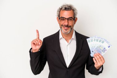 Elinde banknotlar tutan orta yaşlı bir iş adamı mavi arka planda bir numarayı parmağıyla gösteriyor..