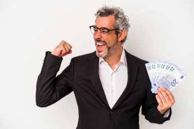 Orta yaşlı iş adamı elinde banknotları mavi arka planda tutuyor zafer kazandıktan sonra yumruğunu kaldırıyor, kazanan konsept.