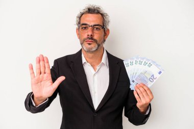 Orta yaşlı bir iş adamı mavi arka planda izole edilmiş banknotlar tutuyor. Elini uzatmış, dur işareti gösteriyor..