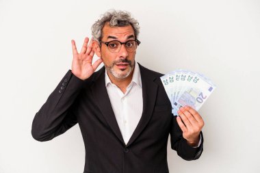 Orta yaşlı iş adamı elinde banknotlarla mavi arka planda bir dedikoduyu dinlemeye çalışıyor..