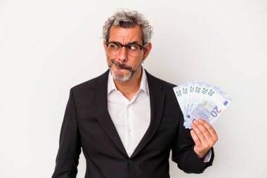 Orta yaşlı bir iş adamı mavi arka planda izole edilmiş banknotlar tutuyor. Kafası karışmış, şüpheli ve kararsız hissediyor..