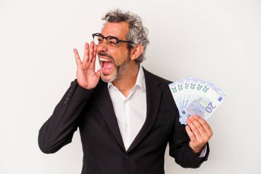 Orta yaşlı bir iş adamı mavi arka planda izole edilmiş banknotlar tutuyor bağırıyor ve avuç içini açık tutuyor..