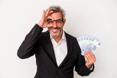 Elinde banknotlar tutan orta yaşlı bir iş adamı mavi arka planda heyecanlı..