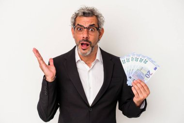 Elinde banknotlar tutan orta yaşlı bir iş adamı mavi arka planda şaşırmış ve şok olmuştu..