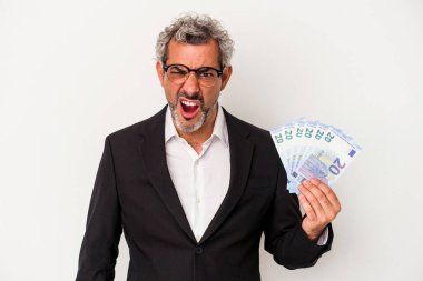 Elinde banknotlar tutan orta yaşlı bir iş adamı mavi arka planda çok sinirli ve agresif çığlıklar atıyor..