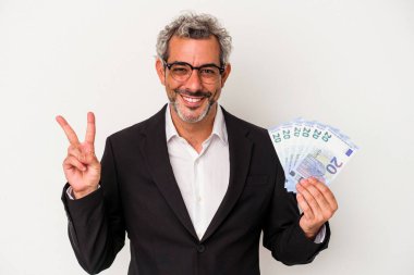 Elinde banknotlar tutan orta yaşlı bir iş adamı mavi arka planda iki numarayı parmaklarıyla gösteriyor..