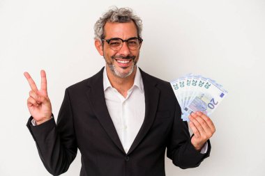 Elinde banknotlar tutan orta yaşlı bir işadamı mavi arka planda neşeli ve kaygısız parmakları olan bir barış sembolü gösteriyor..