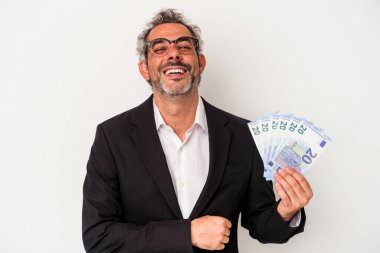 Orta yaşlı iş adamı elinde banknotlarla mavi arka planda gülüp eğleniyor..