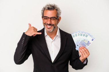 Elinde banknotlar tutan orta yaşlı bir işadamı mavi arka planda parmakları olan bir cep telefonu jesti gösteriyor..