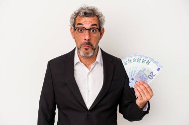 Mavi arka planda izole edilmiş banknotlar tutan orta yaşlı bir iş adamı omuzlarını silker ve gözleri açık kalır..