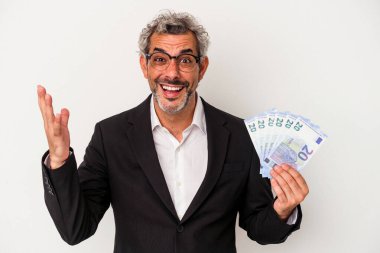Orta yaşlı bir iş adamı mavi arka planda izole edilmiş banknotlar tutuyor. Hoş bir sürpriz alıyor, heyecanlı ve el kaldırıyor..