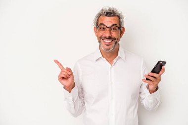 Beyaz arka planda izole edilmiş bir cep telefonu tutan Kafkasyalı iş adamı gülümsüyor ve boş alanda bir şey gösteriyor..