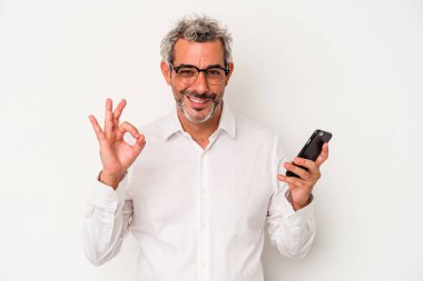 Orta yaşlı beyaz iş adamı beyaz arka planda izole edilmiş bir cep telefonu tutuyor. Neşeli ve kendinden emin..