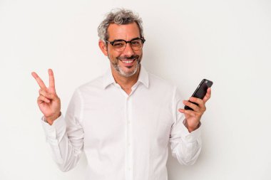 Orta yaşlı beyaz iş adamı beyaz arka planda izole edilmiş bir cep telefonu tutuyor neşeli ve kaygısız parmaklarıyla barış sembolü gösteriyor..