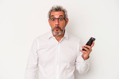 Beyaz arka planda izole edilmiş bir cep telefonu tutan Kafkasyalı iş adamı omuz silkiyor ve gözleri açık..