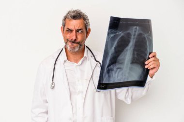 Beyaz arka planda izole edilmiş bir radyografi tutan orta yaşlı bir doktor kafası karışmış ve kendinden emin değil..