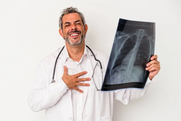 中年医生 一个拿着在白色背景下隔离的放射线的高加索人 大声笑着把手放在胸前 — 图库照片
