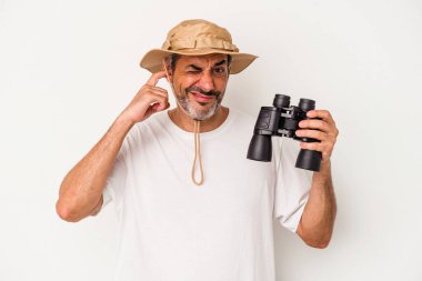 Dürbün tutan orta yaşlı beyaz bir adam beyaz arka planda izole edilmiş kulakları elleriyle kapatıyor..