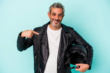 Mavi arka planda izole edilmiş kasklı orta yaşlı motorcu beyaz adam gömlek fotokopi alanını gösteriyor, gururlu ve kendinden emin.
