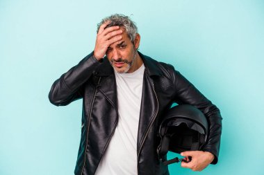 Mavi arka planda kask takan orta yaşlı motorcu beyaz adam şoka uğruyor, önemli bir buluşmayı hatırlıyor..