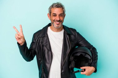 Kasklı orta yaşlı beyaz bir adam mavi arka planda izole edilmiş neşeli ve tasasız parmakları olan barış sembolü gösteriyor..