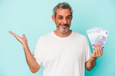 Elinde banknotlar tutan orta yaşlı beyaz bir adam mavi arka planda bir fotokopi alanı ve belinde bir el daha olduğunu gösteriyor..