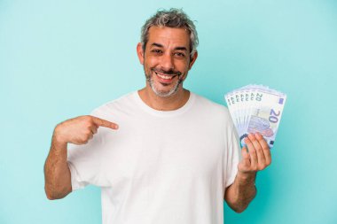 Elinde banknotlar tutan orta yaşlı beyaz bir adam mavi arka planda tek başına gömlek fotokopisini çeken gururlu ve kendinden emin bir adam.