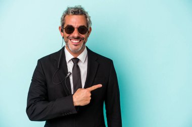 Mavi arka planda izole edilmiş orta yaşlı koruma gülümsüyor ve boş alanda bir şeyler gösteriyor..