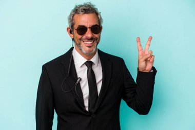 Mavi arka planda izole edilmiş orta yaşlı koruma neşeli ve kaygısız parmaklarıyla barış sembolü gösteren.