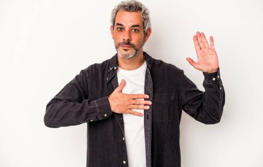 Beyaz arka planda izole edilmiş orta yaşlı beyaz bir adam yemin ediyor, elini göğsüne koyuyor..
