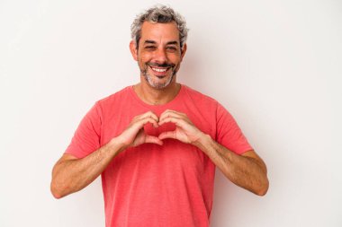 Beyaz arka planda izole edilmiş orta yaşlı beyaz bir adam gülümsüyor ve elleriyle kalp şeklini gösteriyor..