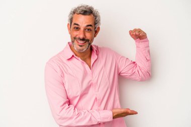 Beyaz arka planda izole edilmiş orta yaşlı beyaz bir adam işaret parmaklarıyla küçük bir şey tutuyor, gülümsüyor ve kendinden emin..