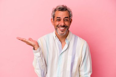 Pembe arka planda izole edilmiş orta yaşlı beyaz bir adam bir palmiye üzerinde fotokopi alanı ve belinde başka bir el tutuyor..